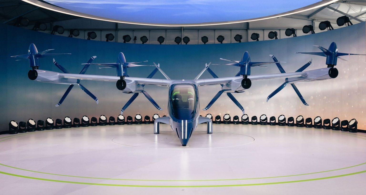 Protótipo de aeronave elétrica com hélices, visto de frente em uma área interna de exposição.