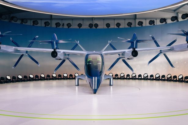 Protótipo de aeronave elétrica com hélices, visto de frente em uma área interna de exposição.