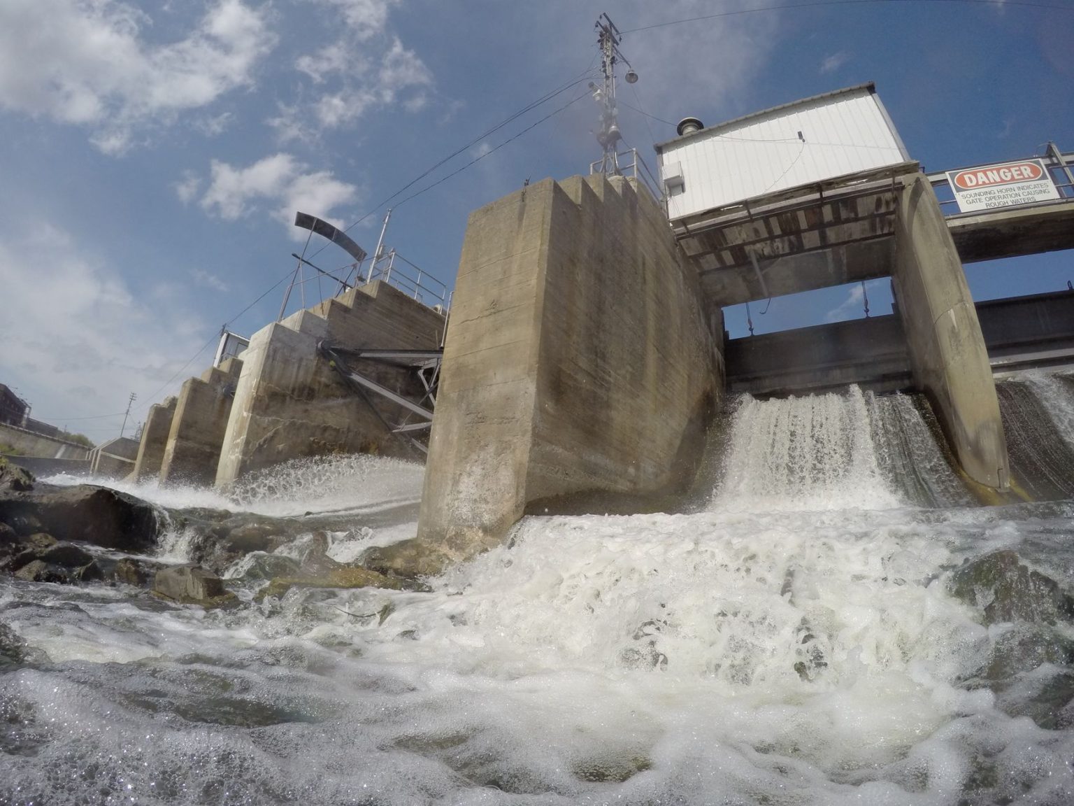 Água escoando sobre uma barragem de concreto sob luz intensa.