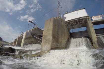 Água escoando sobre uma barragem de concreto sob luz intensa.