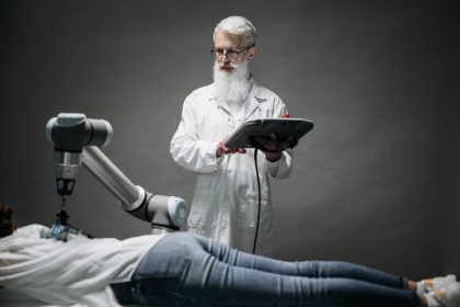Cientista monitora um braço robótico enquanto realiza pesquisa com uma pessoa deitada.