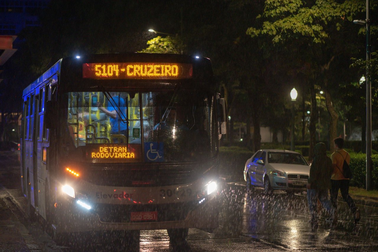 Ônibus urbano circula à noite sob chuva em uma via de Belo Horizonte.