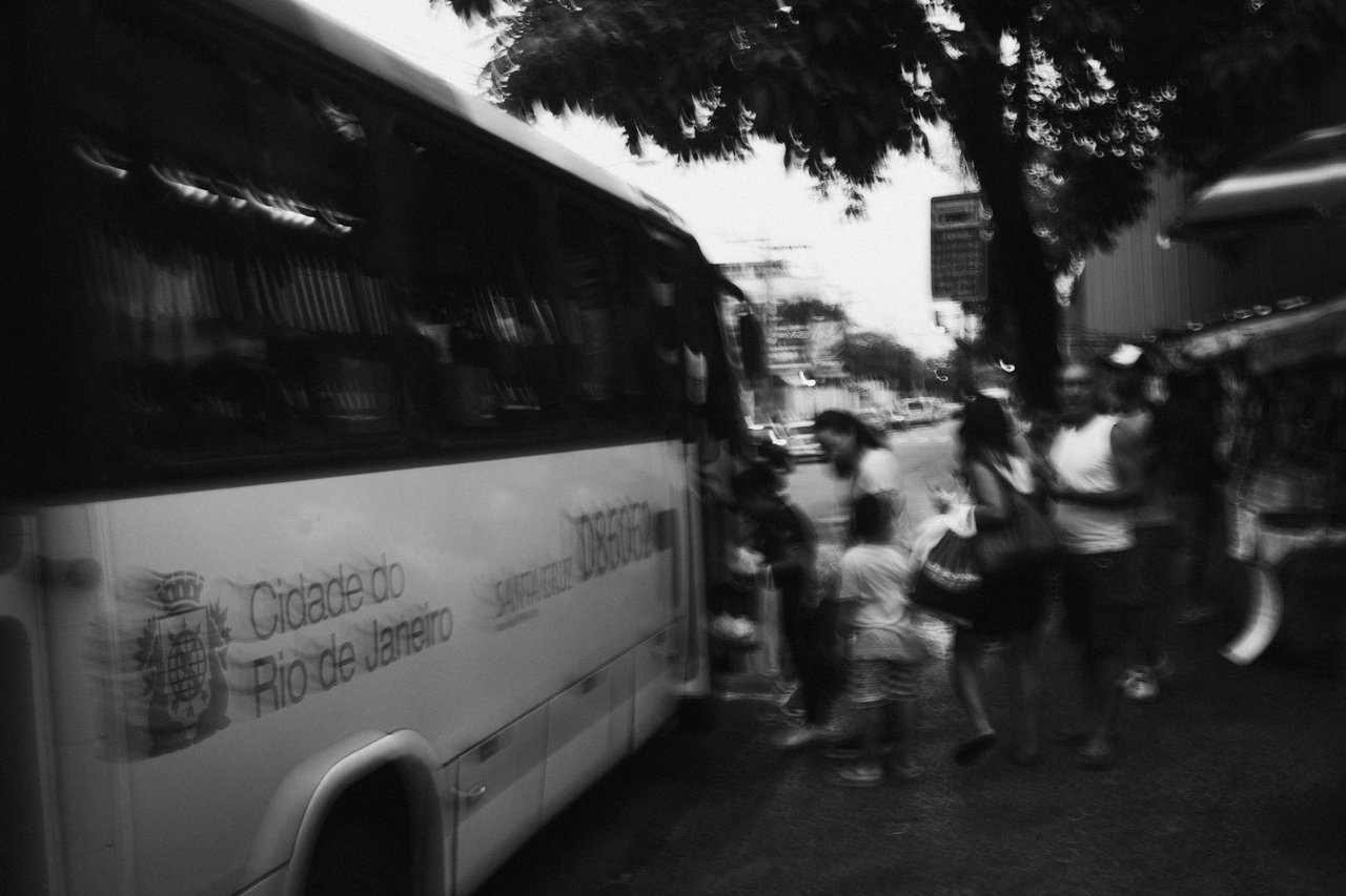Passageiros embarcam em um ônibus urbano no Rio de Janeiro, em fotografia em preto e branco com efeito desfocado.
